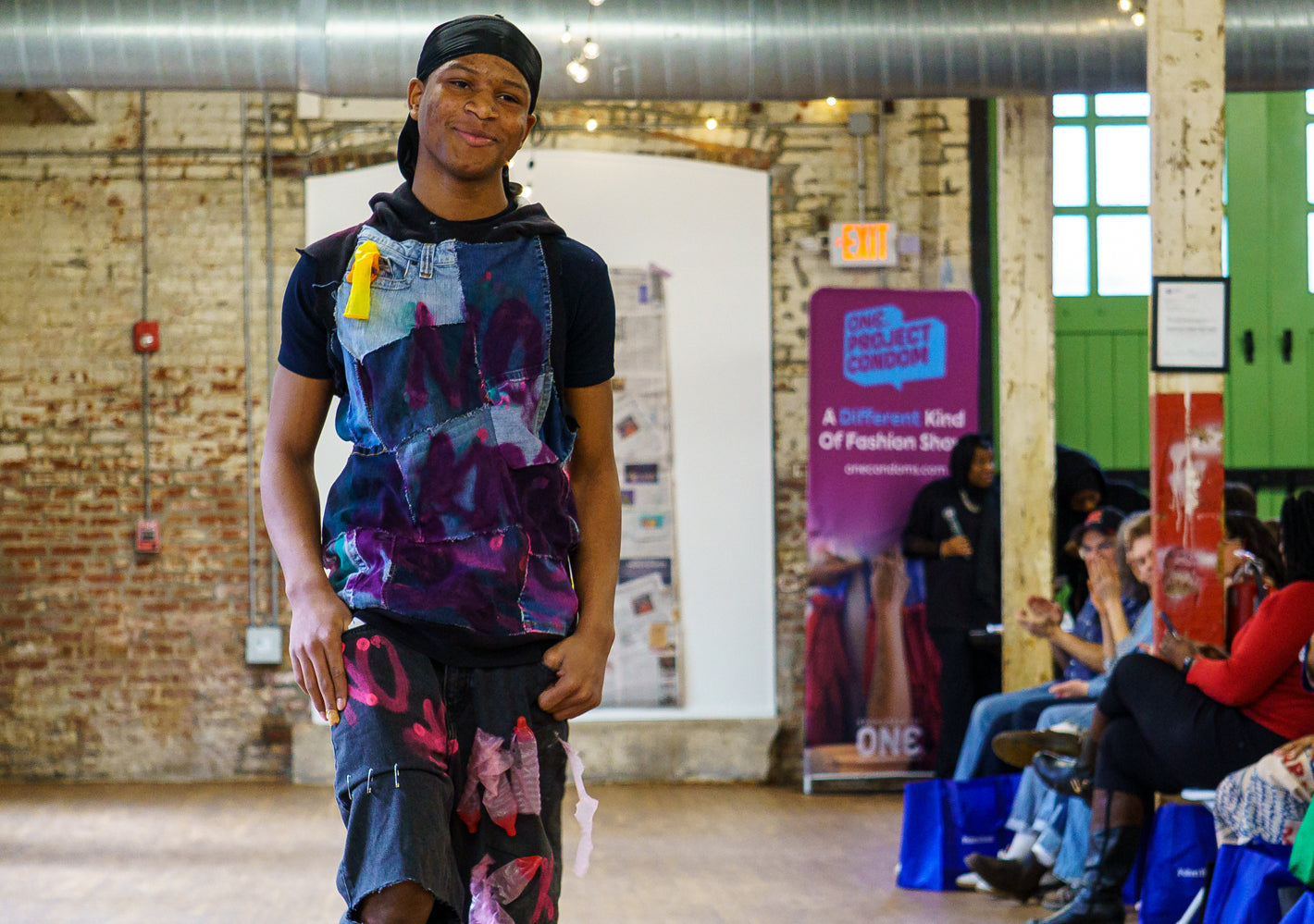 Youth model walking the runway in condom couture garments at Prevention Meets Fashion show with ONE® Project Condom banner in the background