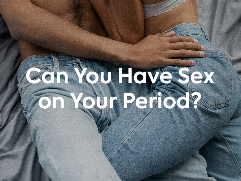 Blog banner for Can You Have Sex on Your Period? Image of couple cuddling in bed with jeans on and text that says "Can You Have Sex on Your Period?"