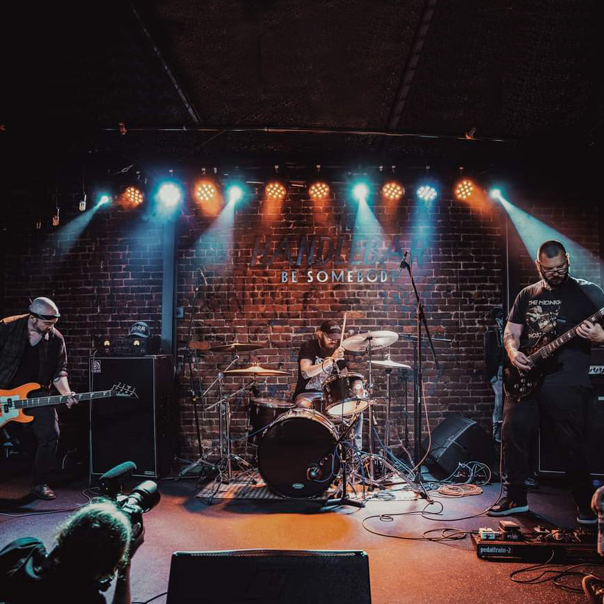 Image of Gnarled - a ONE on Stage band. Band on stage, two members playing guitar and one person playing drums.