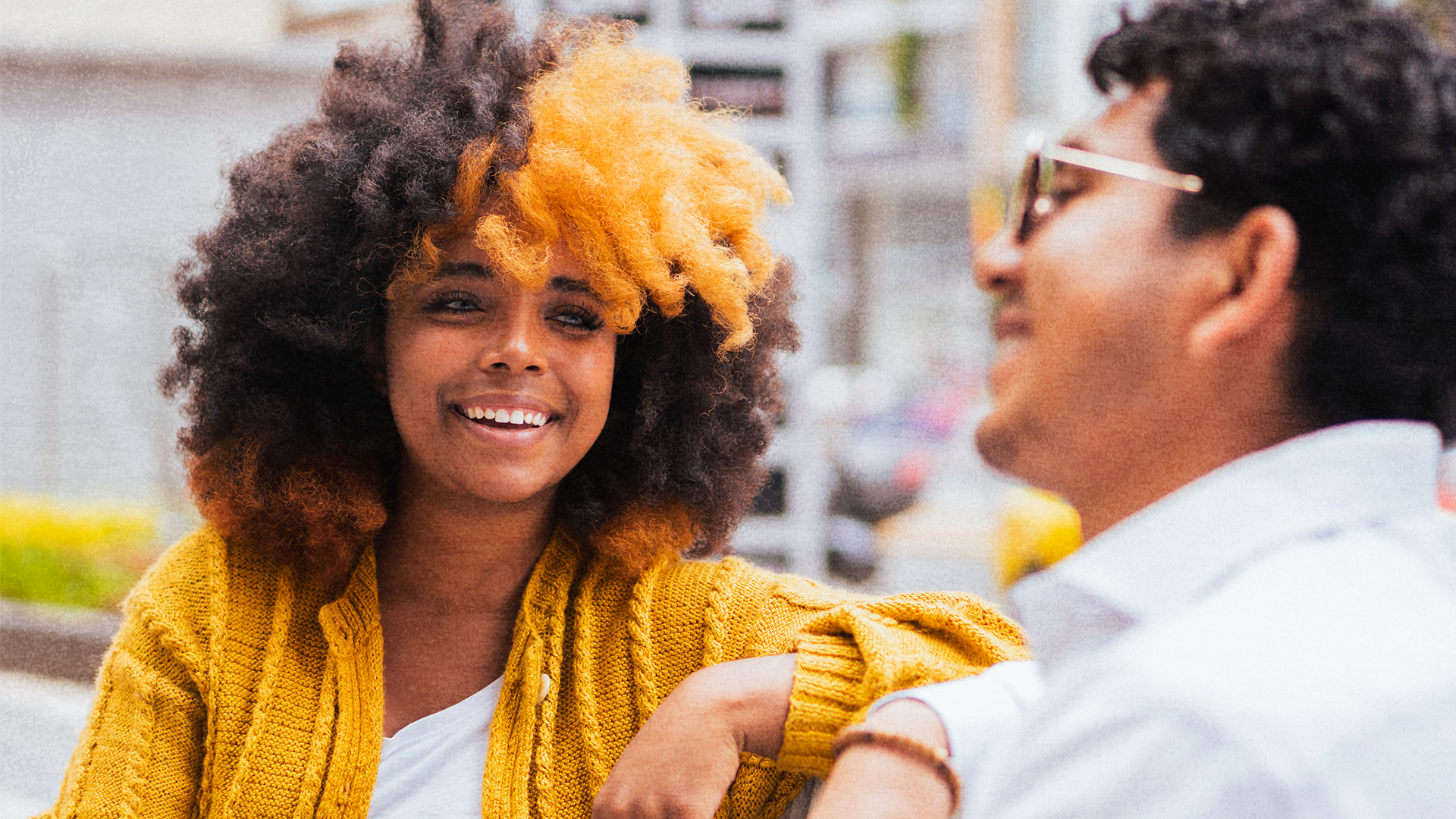 Woman with curly hair and a man having a friendly conversation outdoors.