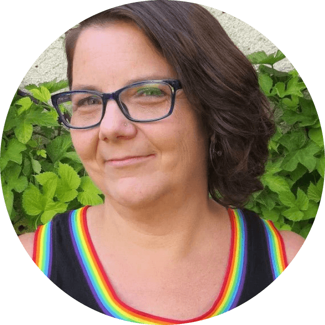 Person wearing glasses and a rainbow striped shirt with greenery in the background